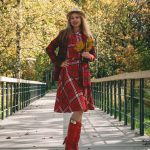 Woman in a red plaid dress holding autumn leaves on a park bridge during fall.