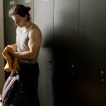 A fit young man with a duffel bag in a locker room, ready for a workout session.